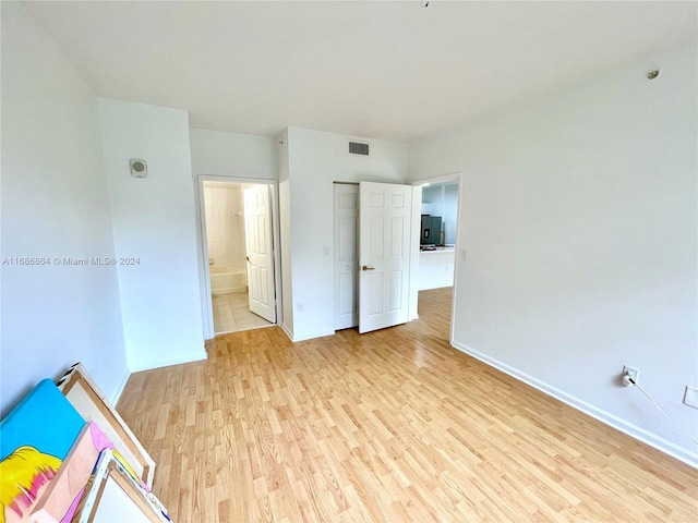 unfurnished bedroom featuring light hardwood / wood-style floors, refrigerator with ice dispenser, and ensuite bath