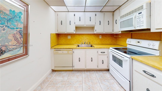 kitchen featuring white appliances, sink, a paneled ceiling, white cabinets, and light tile patterned floors