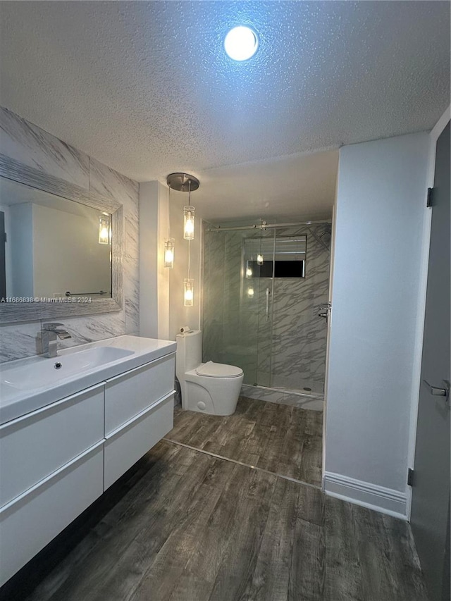 bathroom with a shower with door, toilet, wood-type flooring, vanity, and a textured ceiling