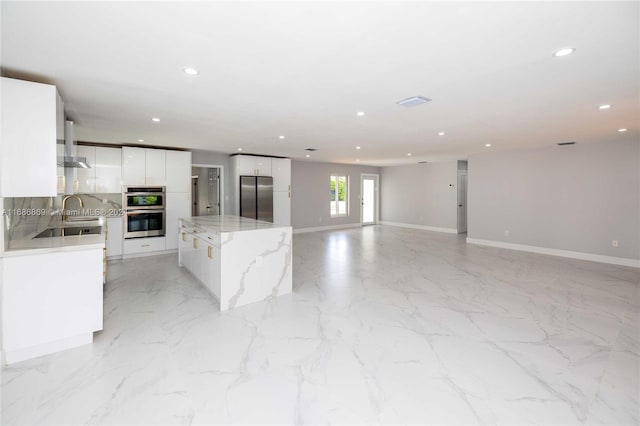 kitchen featuring white cabinets, sink, appliances with stainless steel finishes, a kitchen island, and light stone counters