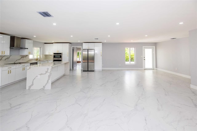 kitchen with tasteful backsplash, white cabinetry, wall chimney range hood, and appliances with stainless steel finishes