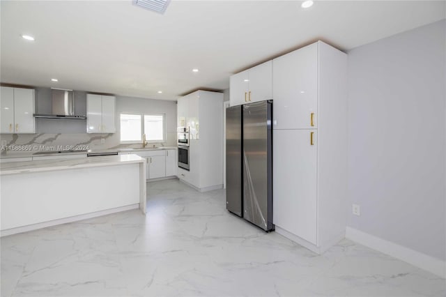 kitchen featuring sink, wall chimney range hood, tasteful backsplash, white cabinets, and appliances with stainless steel finishes