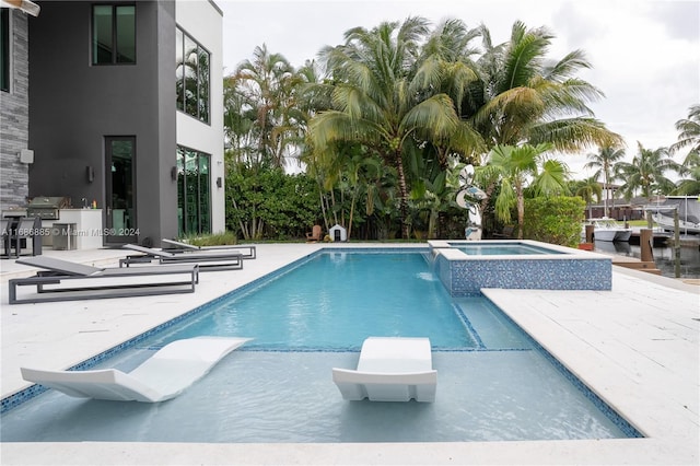 view of swimming pool featuring an in ground hot tub, a patio, an outdoor kitchen, and a grill