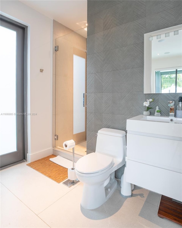 bathroom featuring tile patterned floors, toilet, a shower with door, vanity, and tile walls