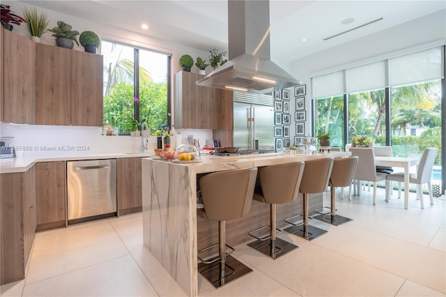 kitchen featuring a breakfast bar area, island range hood, light tile patterned flooring, and stainless steel appliances