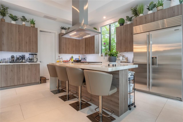 kitchen with a breakfast bar, island range hood, light tile patterned flooring, and appliances with stainless steel finishes