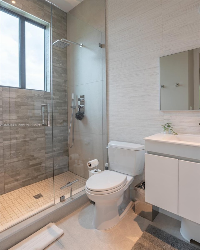 bathroom with vanity, a shower with door, tile patterned flooring, toilet, and tile walls