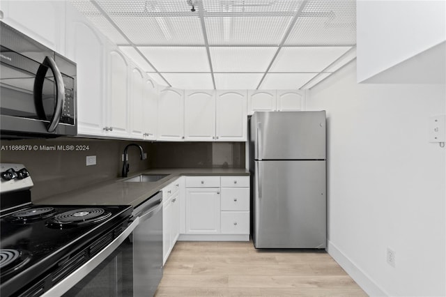 kitchen with light wood-type flooring, backsplash, stainless steel appliances, sink, and white cabinets