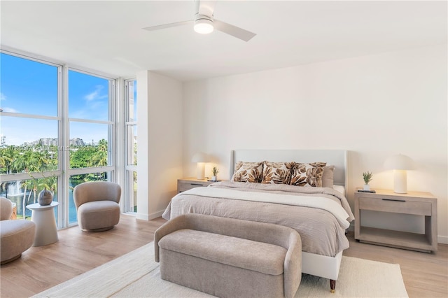 bedroom with baseboards, floor to ceiling windows, a city view, wood finished floors, and a ceiling fan