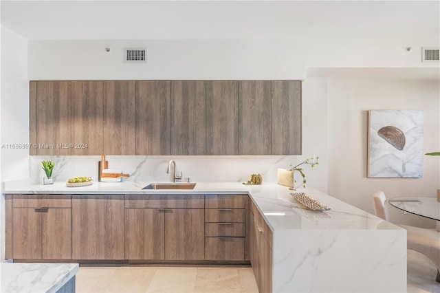 kitchen featuring kitchen peninsula, light tile patterned floors, light stone countertops, and sink