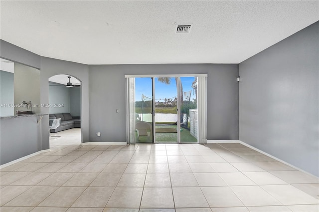 spare room featuring a textured ceiling, light tile patterned flooring, a water view, and ceiling fan