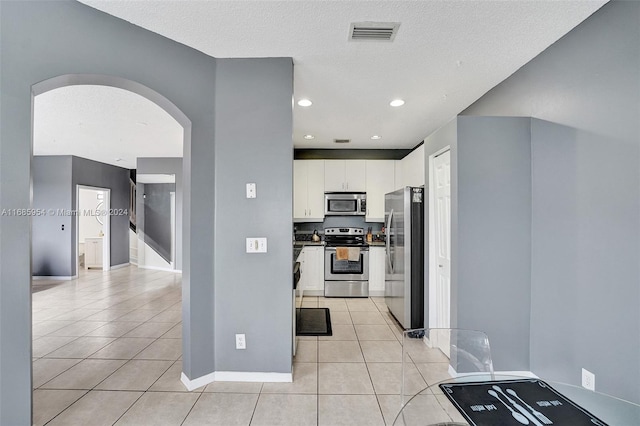 kitchen with stainless steel appliances, a textured ceiling, light tile patterned floors, and white cabinets