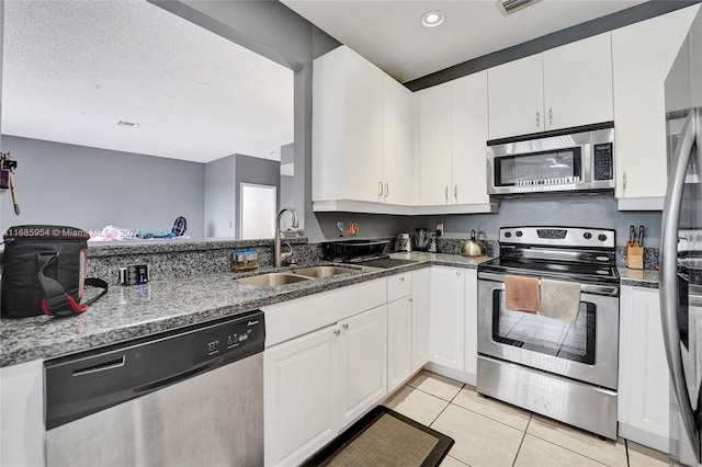 kitchen featuring appliances with stainless steel finishes, white cabinets, dark stone countertops, and sink