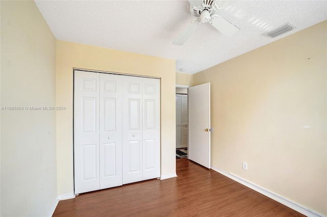 unfurnished bedroom with dark wood-type flooring, a textured ceiling, a closet, and ceiling fan