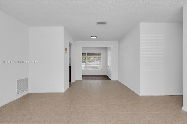 hall with a textured ceiling and light tile patterned floors