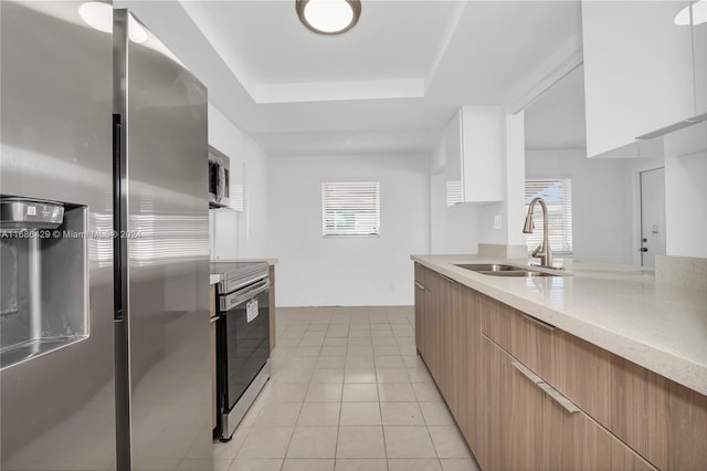 kitchen with appliances with stainless steel finishes, white cabinets, sink, and a raised ceiling