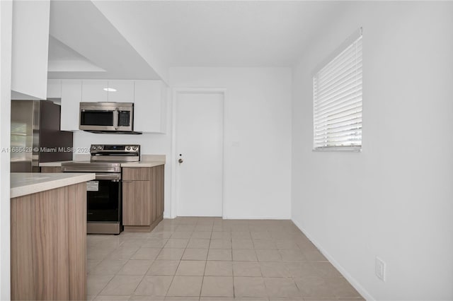 kitchen featuring stainless steel appliances, light tile patterned flooring, and white cabinets