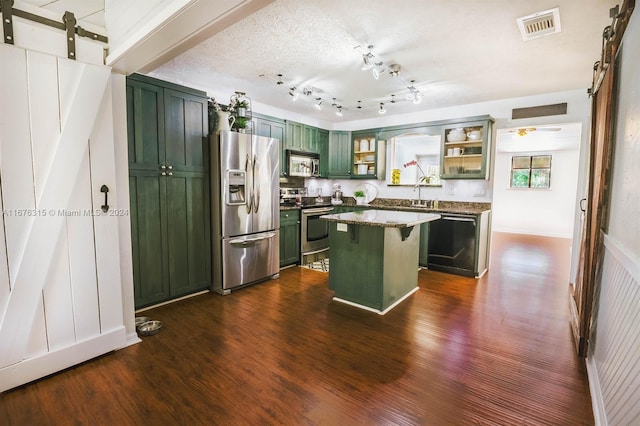 kitchen with a kitchen island, dark hardwood / wood-style floors, stainless steel appliances, a barn door, and a textured ceiling