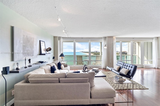 living room with track lighting, hardwood / wood-style flooring, a water view, a textured ceiling, and floor to ceiling windows