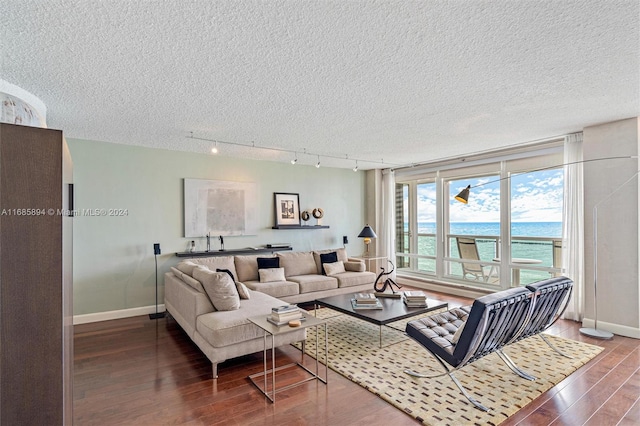 living room with a textured ceiling, a water view, rail lighting, and hardwood / wood-style flooring