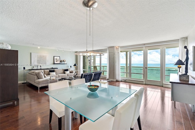 dining space with dark wood-type flooring, rail lighting, a water view, and a textured ceiling