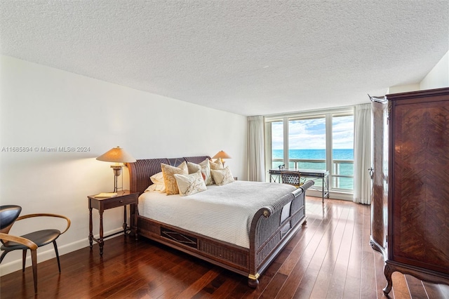 bedroom with a textured ceiling, a water view, and dark hardwood / wood-style floors