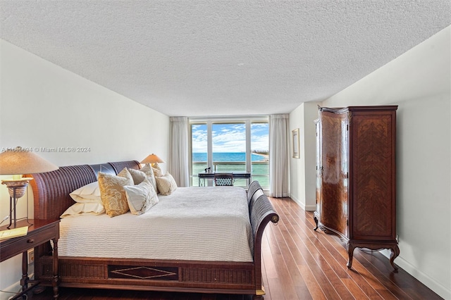 bedroom featuring a wall of windows, a textured ceiling, hardwood / wood-style flooring, and a water view