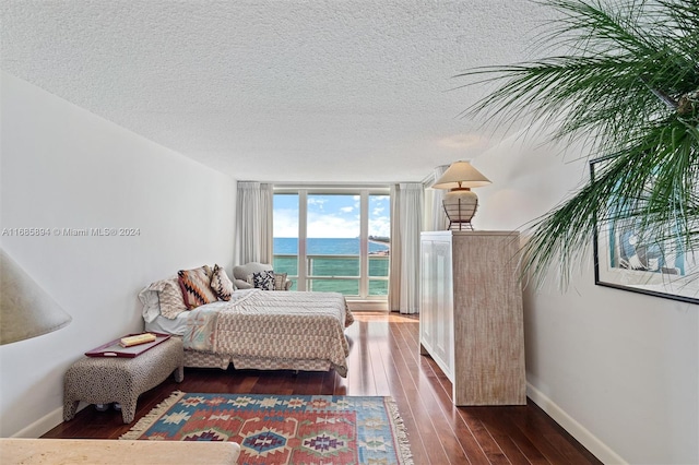 bedroom featuring a water view, a textured ceiling, dark hardwood / wood-style flooring, and floor to ceiling windows