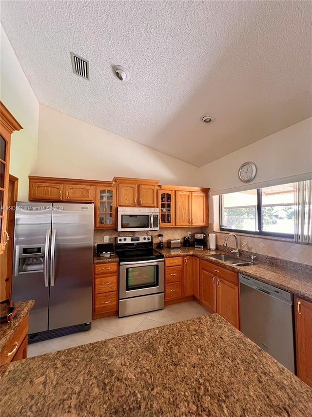 kitchen with lofted ceiling, stainless steel appliances, sink, light tile patterned flooring, and a textured ceiling