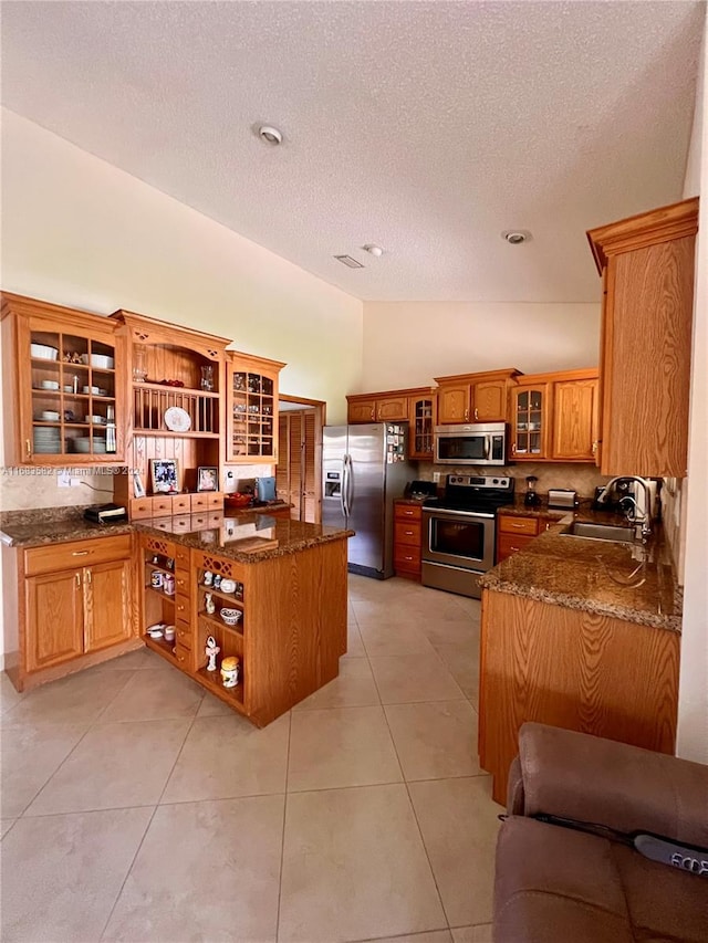 kitchen featuring stainless steel appliances, dark stone countertops, sink, vaulted ceiling, and light tile patterned floors