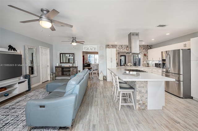 kitchen featuring island exhaust hood, ceiling fan, white cabinetry, light hardwood / wood-style floors, and stainless steel appliances