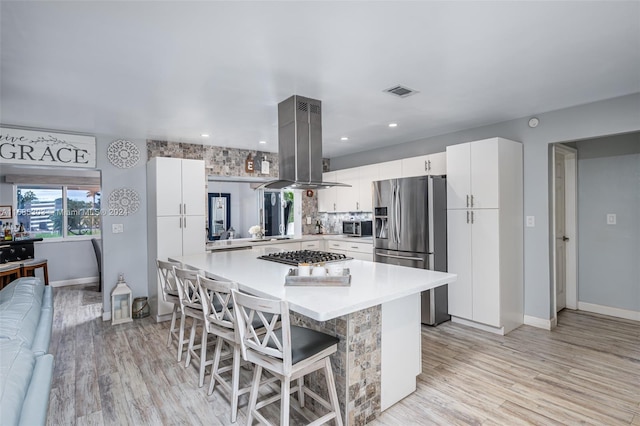 kitchen with island exhaust hood, stainless steel appliances, a kitchen bar, light wood-type flooring, and white cabinetry