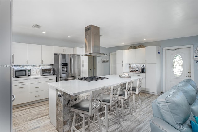 kitchen featuring decorative backsplash, appliances with stainless steel finishes, white cabinetry, island range hood, and light hardwood / wood-style flooring