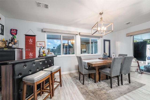 dining room featuring an inviting chandelier, bar area, light hardwood / wood-style floors, and a healthy amount of sunlight