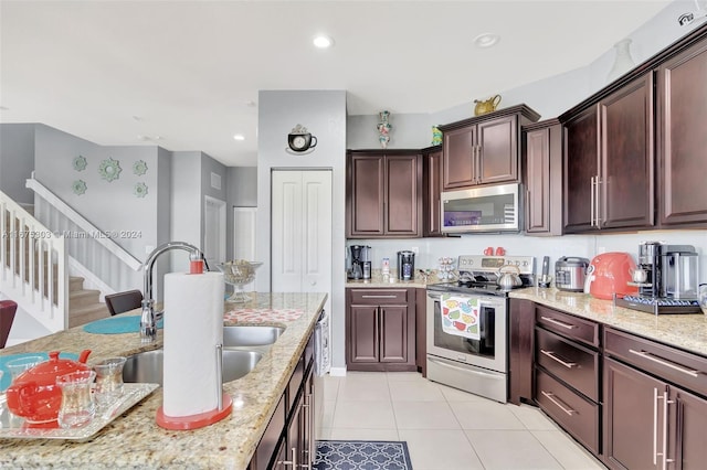 kitchen with light stone countertops, appliances with stainless steel finishes, dark brown cabinets, sink, and light tile patterned floors