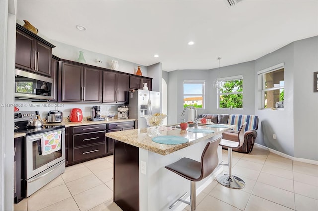 kitchen featuring pendant lighting, a breakfast bar, a center island with sink, appliances with stainless steel finishes, and light stone counters