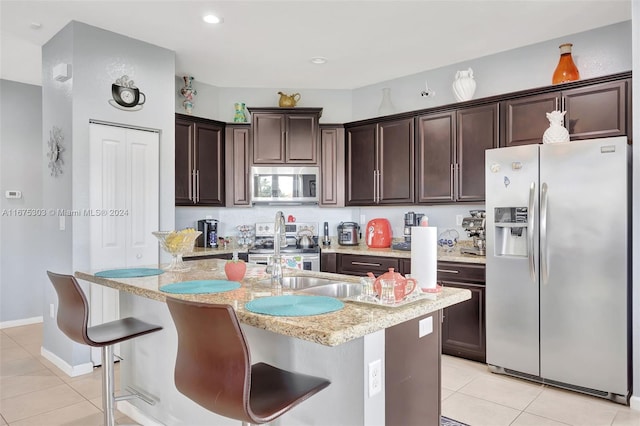 kitchen with a kitchen breakfast bar, light tile patterned flooring, stainless steel appliances, and an island with sink