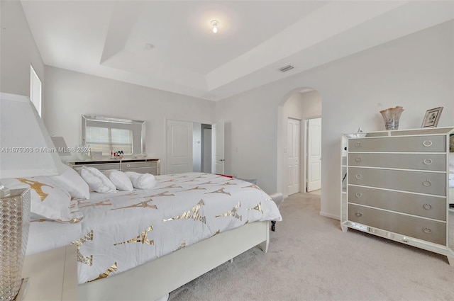 bedroom with a raised ceiling and light colored carpet