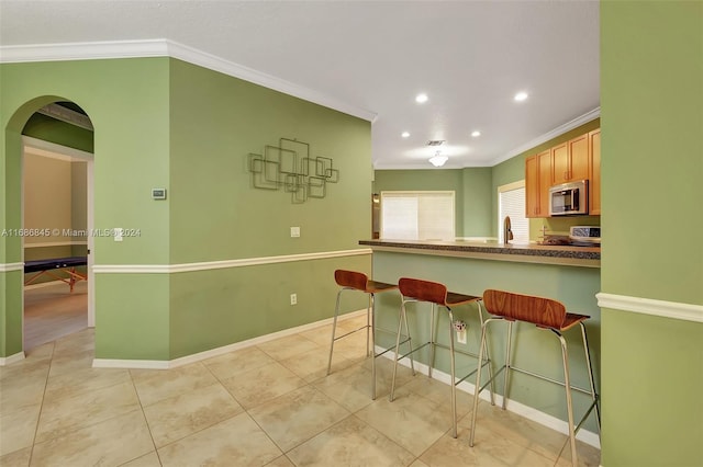 kitchen featuring sink, kitchen peninsula, a kitchen breakfast bar, stainless steel appliances, and crown molding