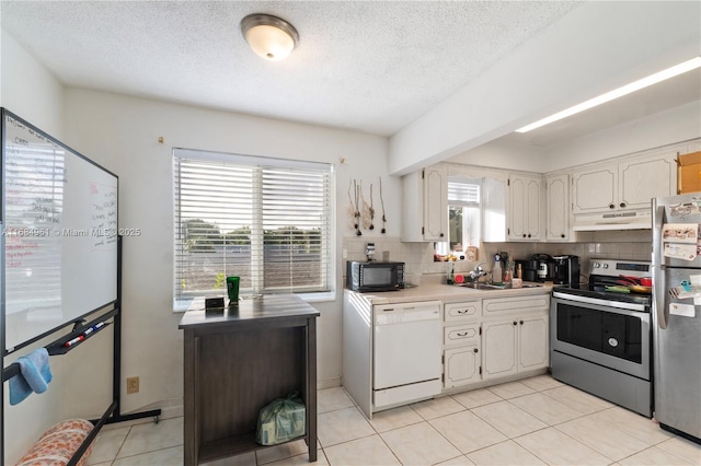 kitchen with light tile patterned floors, decorative backsplash, appliances with stainless steel finishes, a sink, and under cabinet range hood