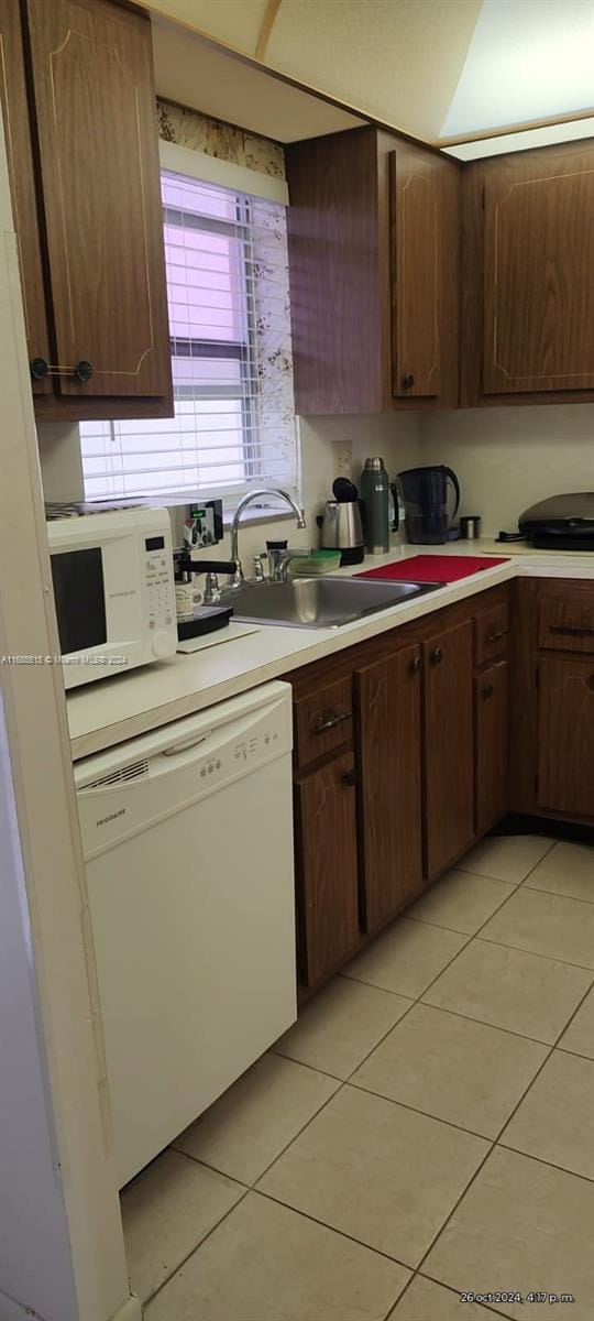 kitchen with white appliances, dark brown cabinetry, light tile patterned flooring, and sink