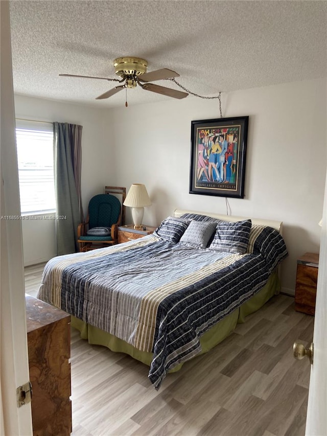 bedroom with a textured ceiling, wood-type flooring, and ceiling fan