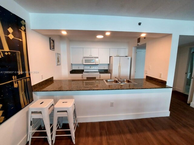 kitchen featuring white cabinets, kitchen peninsula, dark wood-type flooring, and white appliances