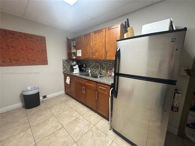 kitchen featuring sink, a paneled ceiling, stainless steel fridge, stone counters, and backsplash