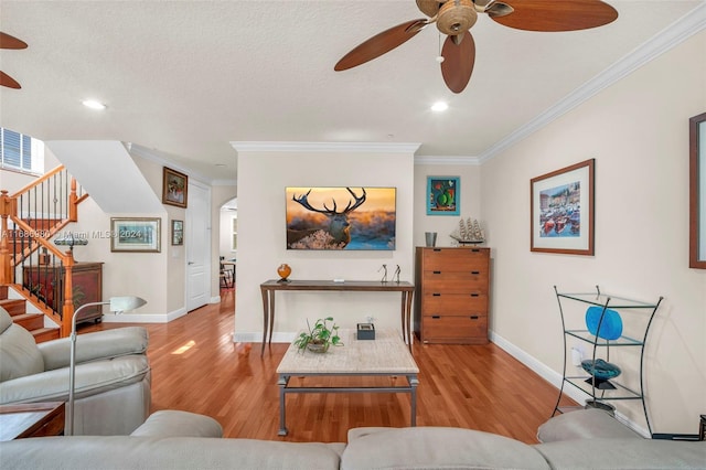 living room with ceiling fan, a textured ceiling, ornamental molding, and light hardwood / wood-style flooring