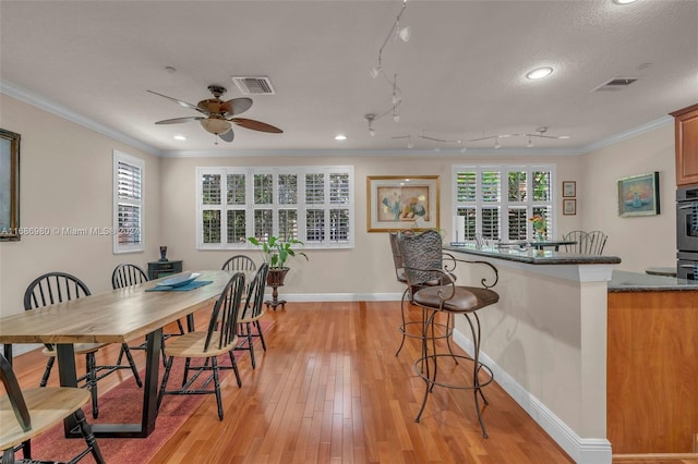 dining room featuring light hardwood / wood-style floors, ornamental molding, a textured ceiling, and ceiling fan