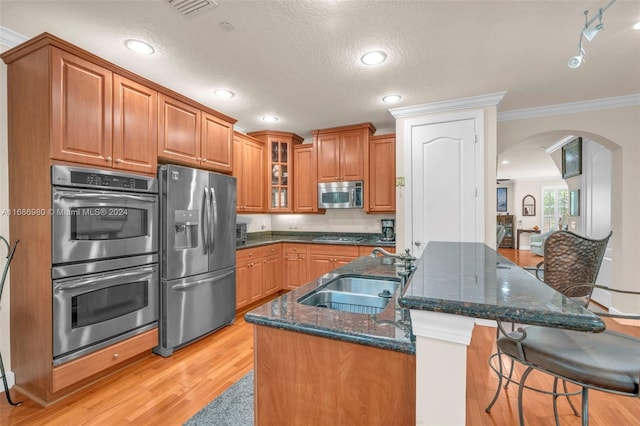 kitchen featuring appliances with stainless steel finishes, a textured ceiling, dark stone counters, ornamental molding, and sink