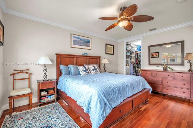 bedroom featuring a closet, a walk in closet, ornamental molding, hardwood / wood-style floors, and ceiling fan