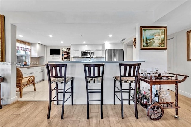 kitchen with appliances with stainless steel finishes, sink, a kitchen bar, white cabinetry, and light hardwood / wood-style flooring