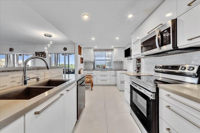 kitchen with tasteful backsplash, appliances with stainless steel finishes, sink, white cabinetry, and decorative light fixtures